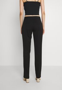 Pantalons noirs ajustés avec une coupe droite, poches arrière et une texture lisse, associés à un haut noir court et des chaussures à talons block beiges.