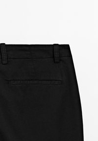 Pantalons noirs avec une texture lisse, passants de ceinture et une seule poche arrière avec une fente horizontale. Coupe épurée sans motifs visibles.