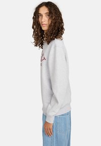 Sudadera gris con un ajuste relajado, puños acanalados y un logo burdeos en el frente. Combinada con jeans de mezclilla azul con un patrón texturizado.