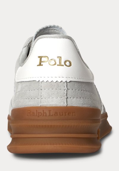 Pilkas zomšinis sportbačio galinis vaizdas su baltu odiniu kulno lopinėliu, auksiniu „Polo“ logotipu ir ruda guminė pada su įspaustu „Ralph Lauren“.