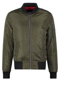 Olivově zelená bomber bunda s černým límcem, manžetami, spodním lemem, předním zipem, kapsou na zip na rukávu a červenou podšívkou.