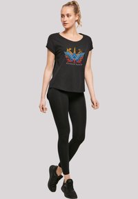 Svart t-skjorte med kort erme med en fargerik Wonder Woman-logo, parret med svarte leggings og svarte joggesko.