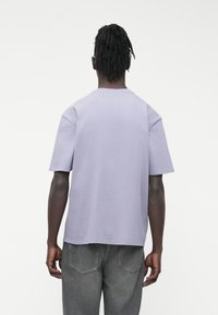 Gaiši violetas krāsas kokvilnas T-krekls ar īsām piedurknēm un apaļu izgriezumu, valkāts kopā ar pelēkiem džinsa biksēm. Vienkāršs, ērtas piegriezuma dizains bez rakstiem.