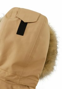 Cappotto invernale beige con cappuccio, rifinito con una bordatura in pelliccia sintetica, cuciture rinforzate e un patch in velcro nero per una chiusura sicura.