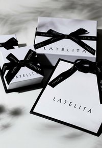 Három fehér ajándékdoboz fekete díszítéssel, szalagokkal, és a "LATELITA" felirat jól láthatóan szerepel minden dobozon.