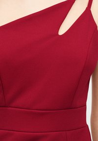 Rode mouwloze jurk met een getailleerde taille en een asymmetrische halslijn met een sleutelgatuitgesneden aan de rechterkant.