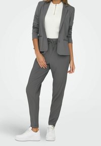 Szary dopasowany żakiet w zestawie z pasującymi spodniami dresowymi. Pod spodem biały zamek na górze, wykończone białymi sneakersami. Teksturowana tkanina, slim fit.