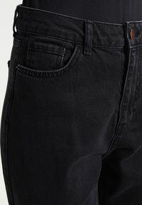 Schwarze Denim-Jeans mit geradem Schnitt, ausgestattet mit einem Knopfverschluss, fünf Taschen und dezenten Nähten. Der Stoff hat eine glatte, leicht strukturierte Oberfläche.