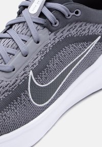 Γκρι και σκούρο γκρι παπούτσι για τρέξιμο Nike με πλεκτό επάνω μέρος, γκρι κορδόνια και λευκή σόλα σε κοντινή εικόνα.