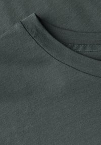 Mörkgrön bomullstyg med en slät textur, som visar en närbild av en rund halsringning och ribbad krage.