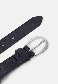 Ceinture en cuir bleu marine avec un motif tissé texturé ; elle est dotée d'une boucle ovale en argent et de plusieurs trous de réglage.