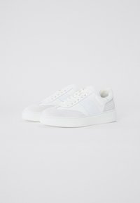 Sneakers bianchi caratterizzati da una combinazione di texture lisce e scamosciate, con una suola spessa e accenti laterali discreti. Design con lacci e dettagli minimi.
