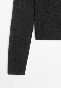 Manica di un maglione lavorato a maglia grigio scuro con una texture a coste e un taglio dritto, senza hardware o modelli visibili.