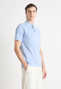 Polo shirt azzurro chiaro con colletto classico, maniche corte e rifiniture bianche sui polsini e sul colletto. Tessuto morbido, design aderente.