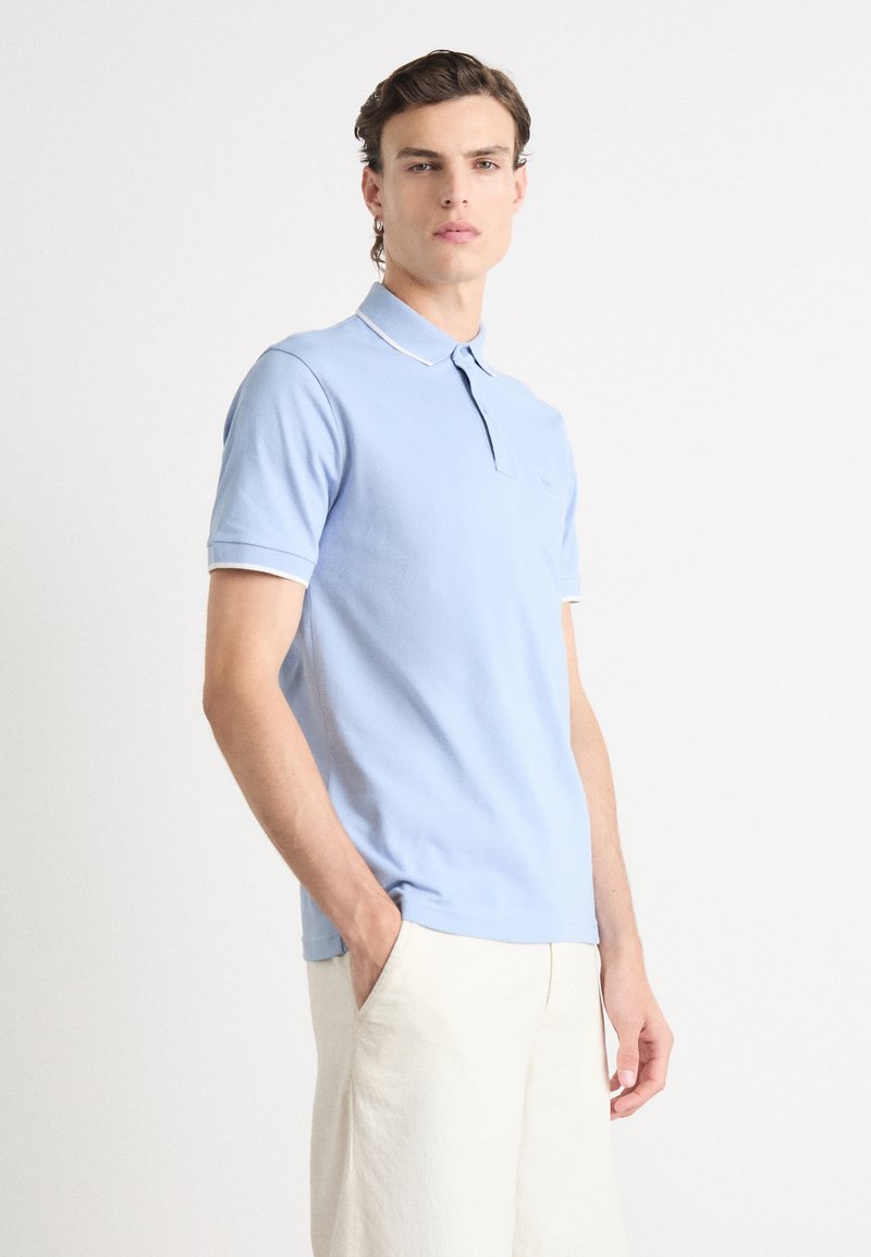 Polo shirt azzurro chiaro con colletto classico, maniche corte e rifiniture bianche sui polsini e sul colletto. Tessuto morbido, design aderente.