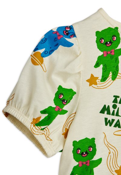 Μανίκι παιδικού κρεμ πουκαμίσου με πράσινες καρτούν αρκούδες που φοράνε ροζ παπιγιόν και πορτοκαλί αστέρια και σπειροειδείς σχεδιασμούς στο ύφασμα.