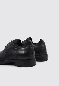 Chaussures en cuir noir avec des orteils arrondis, texture lisse, design à lacets et semelle en caoutchouc basse, présentant des accents minimalistes et un profil élégant.