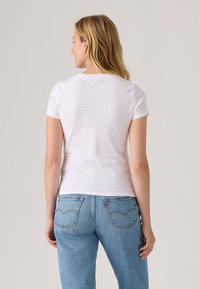 T-shirt branca de manga curta com decote redondo, design ajustado, textura suave e costas simples sem adornos, combinada com jeans azuis.