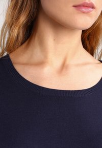 Haut en maille bleu marine avec un grand col arrondi et une texture lisse, mettant l'accent sur la partie supérieure du torse sans détails supplémentaires.