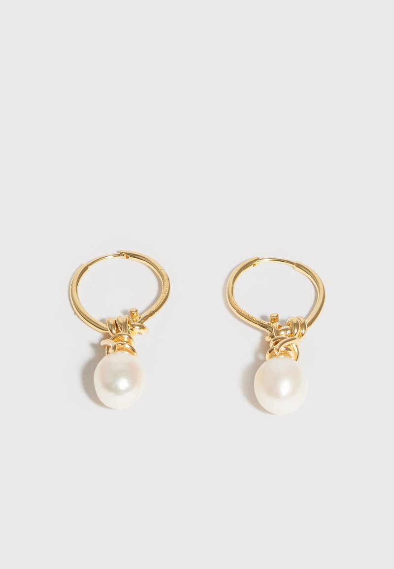 Χρυσά σκουλαρίκια κρίκοι με μία λευκή μαργαριταρένια σταγόνα να κρέμεται από κάθε ένα, εμφανισμένα σε ένα απλό ανοιχτό γκρι φόντο.