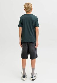 Camiseta de algodón verde, de mangas cortas, combinada con pantalones cortos de mezclilla oscura y calcetines grises. Las zapatillas tienen acentos azules y una suela texturizada.