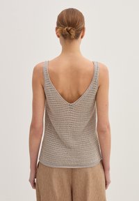 Canotta lavorata a maglia beige chiaro con un profondo scollo a V nella parte posteriore, caratterizzata da un pattern aperto e testurizzato e spalline larghe.