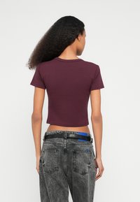 T-shirt cropped de manga curta em algodão bordô profundo com decote redondo. Combinado com jeans pretos gastados de cintura alta, com detalhes em azul.