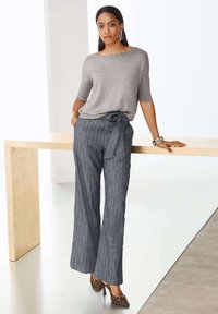 Grijs gebreid topje met zilveren accenten, gecombineerd met wijde marineblauwe gestreepte broeken die op de taille zijn gestrikt. Bruine geprinte hakken maken de outfit af.