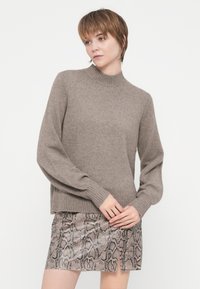 Maglione marrone lavorato a maglia con collo alto e polsini a coste, abbinato a una mini gonna in stampa serpente con dettaglio di spacco laterale.