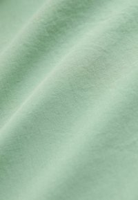 Tissu vert menthe clair avec une surface lisse et légèrement texturée, présentant une qualité douce et respirante ainsi que des variations subtiles de couleur.