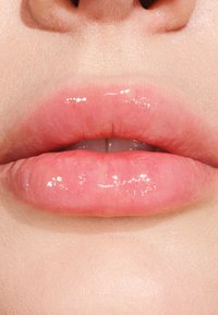 Labbra piene con una finitura lucida, caratterizzate da una sfumatura rosa chiaro e una superficie liscia, leggermente testurizzata. Lo sfondo è minimale e neutro.