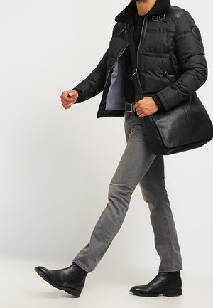 Doudoune noire avec col en shearling, jean gris ajusté et bottines en cuir noires. Portant un sac à bandoulière en cuir noir.