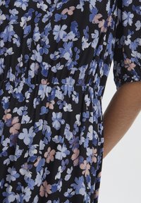 Šaty s květinovým potiskem na tmavě černém pozadí. Obsahují světle modré a broskvové květy, nařasený pas a krátké nabírané rukávy. Jemná textilie.