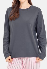 Grå långärmad tröja med rund halsringning, mjukt tyg, avslappnad passform och lätt sidspringor, tillsammans med rosa randiga pyjamasshorts.
