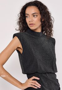 Top negro sin mangas con cuello alto, hecho de una tela texturizada que presenta un sutil brillo. Silueta ajustada con cortes laterales.