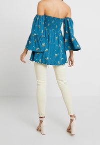 Vihreä olkaimeton paita, jossa on taskuhihat, smokkaukset ja kukkakuosi; yhdistettynä valkoisiin kapeisiin farkkuihin ja nude-väisiin korkokenkiin.