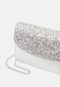 Silver clutch-väska med ett glittrande silverlock, en slät vit kropp och en silverkedjeaxelrem. Texturen är glittrande och reflekterande.