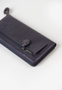 Portafoglio in pelle viola con chiusura a zip, superficie testurizzata e dettaglio con bottone a scatto; presenta un design funzionale con una tasca sicura.