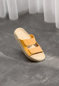 Keltaiset liukusandaalit, joissa on kaksi säädettävää hihnaa, kuvioitu pohja ja sileä pohja. Hihnassa on brändäys.