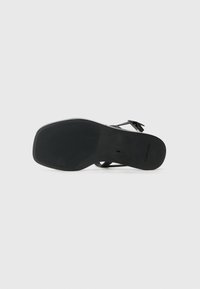 Black sandal with a flat sole, simple strap design, textured rubber bottom, and a logo imprint. Smooth finish with minimal hardware details.