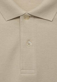 Beige Polohemd mit strukturiertem Strick, dreiknöpfigem Kragen und klassischem Kragen. Die Knöpfe sind hell gefärbt und mit zwei Löchern gestaltet.