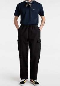 Marineblauw polo shirt met korte mouwen, gecombineerd met losse zwarte cargobroek met zijzakken, en meerkleurige Vans schoenen met een zwarte zool.