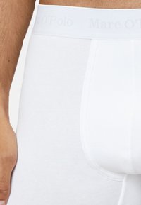 Boxer-culottes blancs en coton avec une ceinture élastique confortable, arborant le logo "Marc O'Polo" dans une impression légère et subtile.