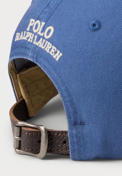 Modrá bavlnená čiapka s bielym vyšívaným logom "POLO RALPH LAUREN", hnedým koženým pásikom so striebornou kovovou sponou, khaki podšívkou viditeľnou vo vnútri.