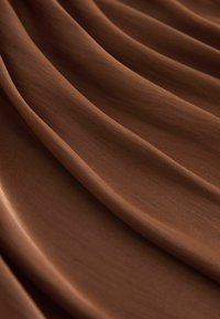 Gros plan sur un tissu marron lisse avec des plis doux et fluides créant de légères ombres et une texture sur toute la surface.