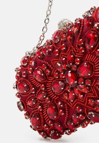 Pochette rouge ornée de perles délicates et de grands détails en gemmes, dotée d'une chaîne en argent et d'une forme arrondie et structurée.