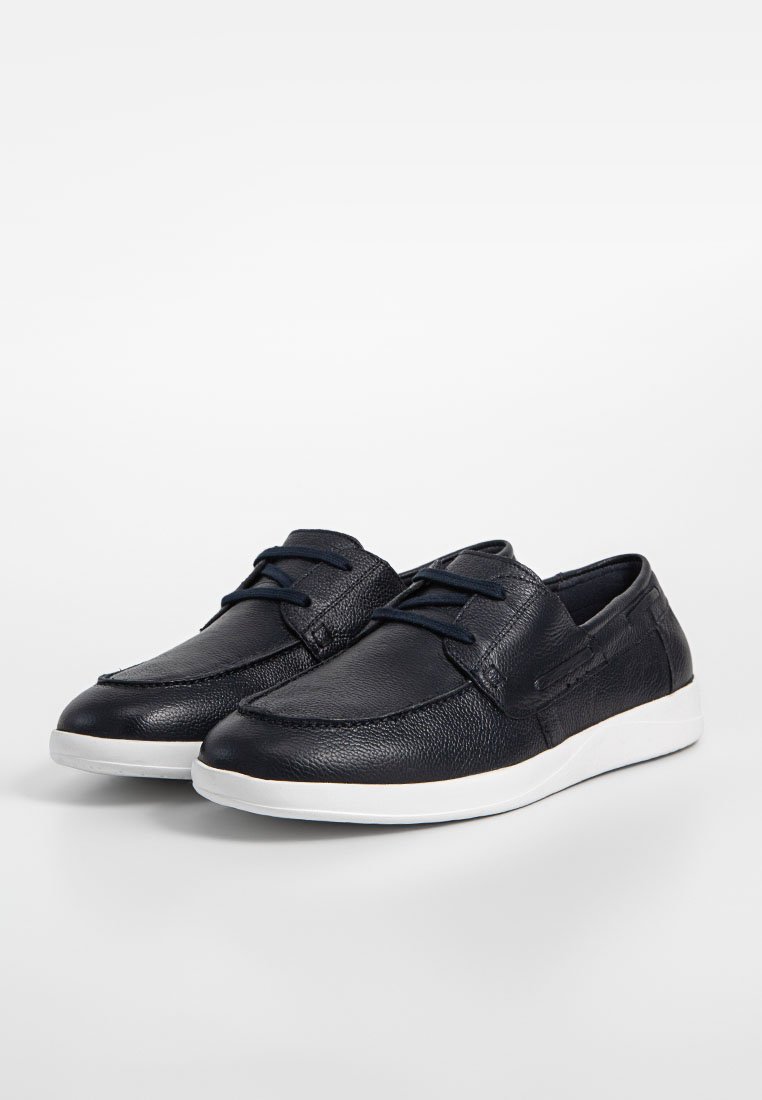 Chaussures en cuir bleu marine avec une finition texturée, bout rond et semelle en caoutchouc blanc. Présente des lacets décoratifs et des accents de couture sur la tige.