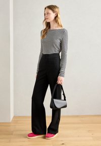 Pantaloni neri a vita alta, maglietta a maniche lunghe bianca e nera a righe, scarpe rosa con suola crema e una piccola borsa nera.