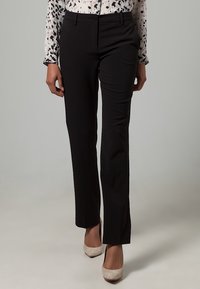 Musta räätälöidyt housut suorilla lahkeilla, sileästä kankaasta, yhdistetty kuvioituun paitaan ja vaaleisiin korkokenkiin.