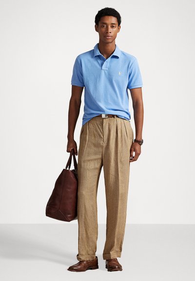 Ανοιχτό μπλε πουκάμισο πόλο, καφέ καρό παντελόνι, καφέ δερμάτινα παπούτσια και καφέ δερμάτινη τσάντα. Το ύφασμα φαίνεται μαλακό με άνετη εφαρμογή.